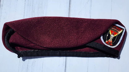 Maroon pouch with a black strap on a light wooden surface