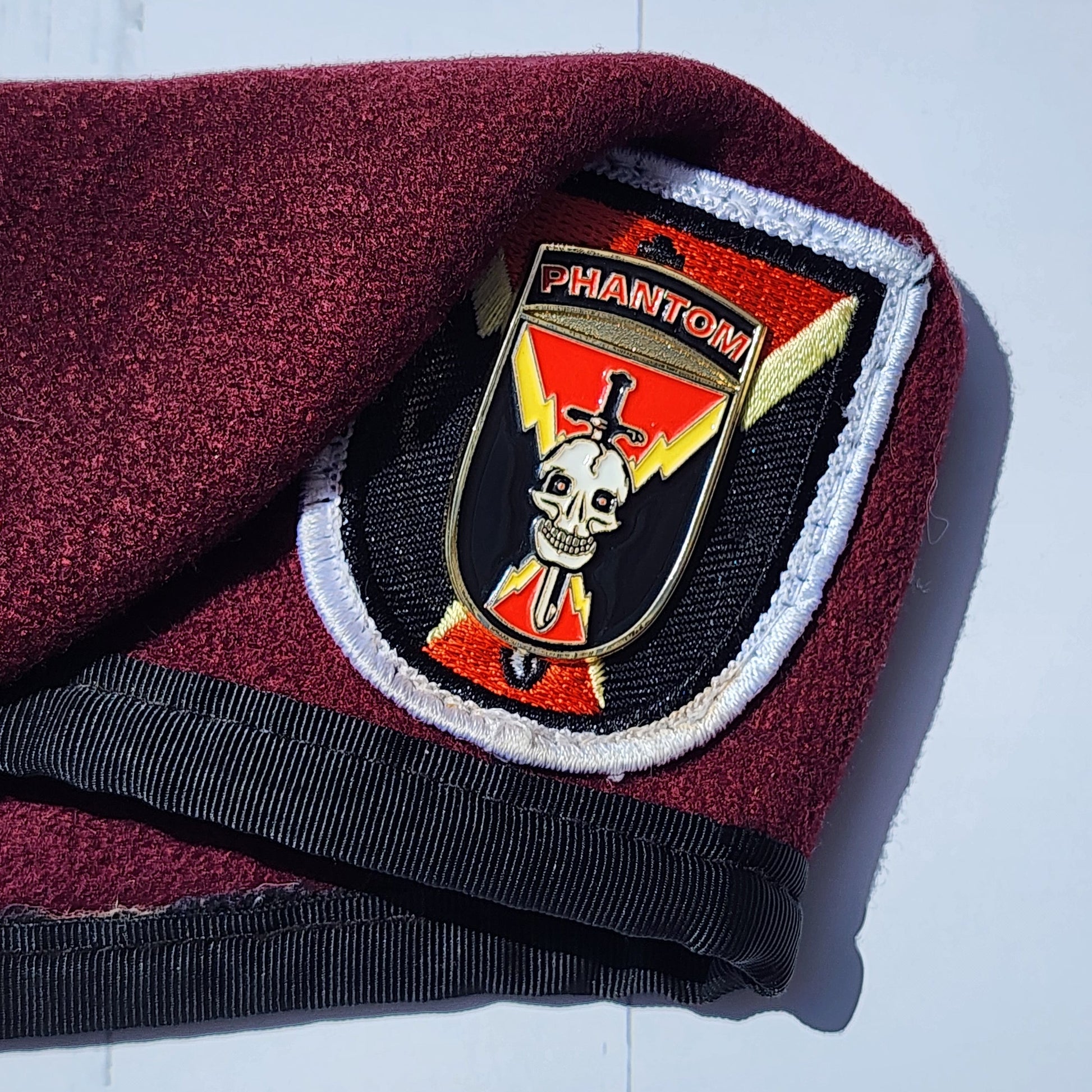 Maroon fabric with a black strap and a decorative badge featuring a skull and crossbones on a white background
