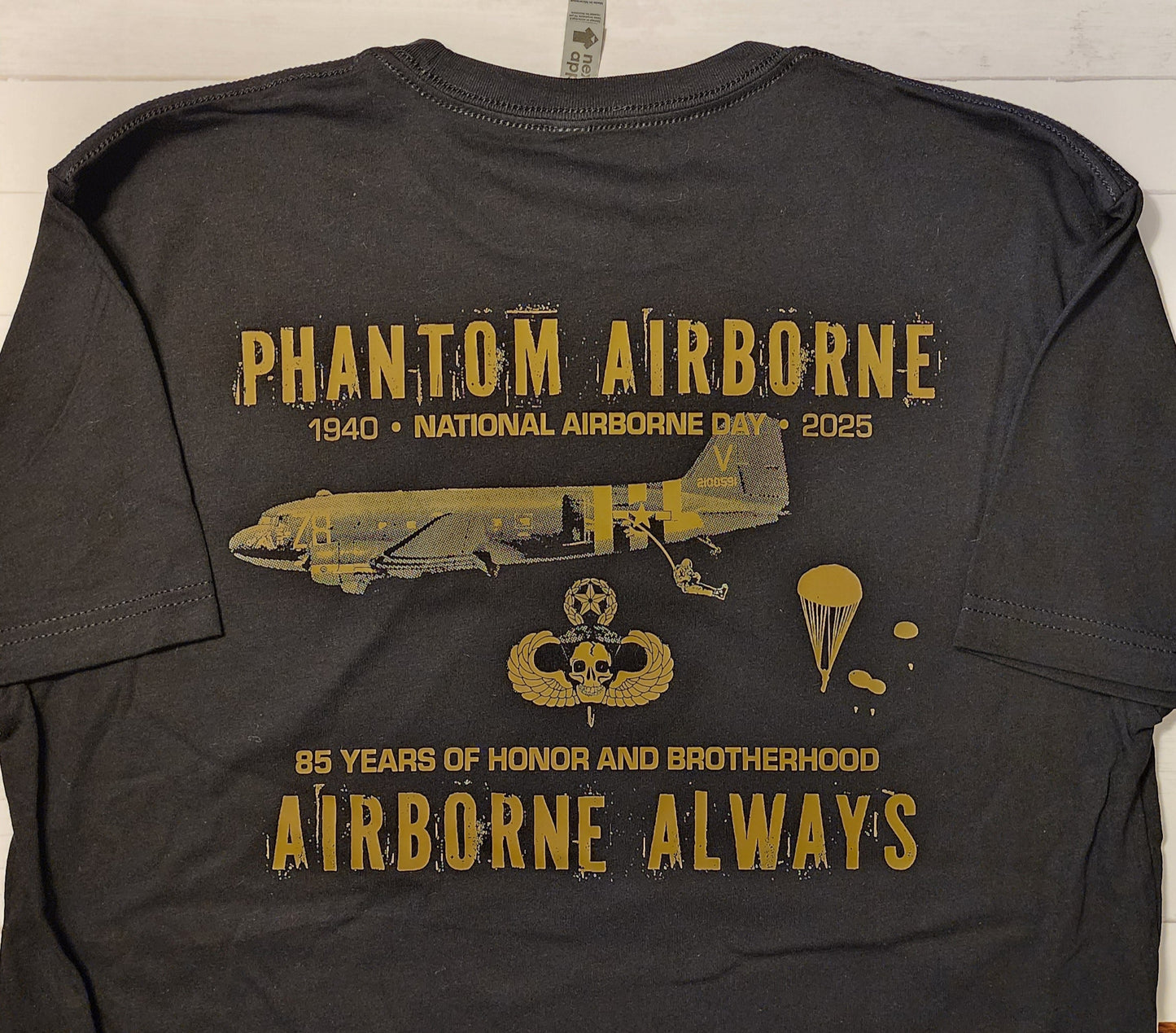 Black t-shirt with gold graphics and text on a wooden surface