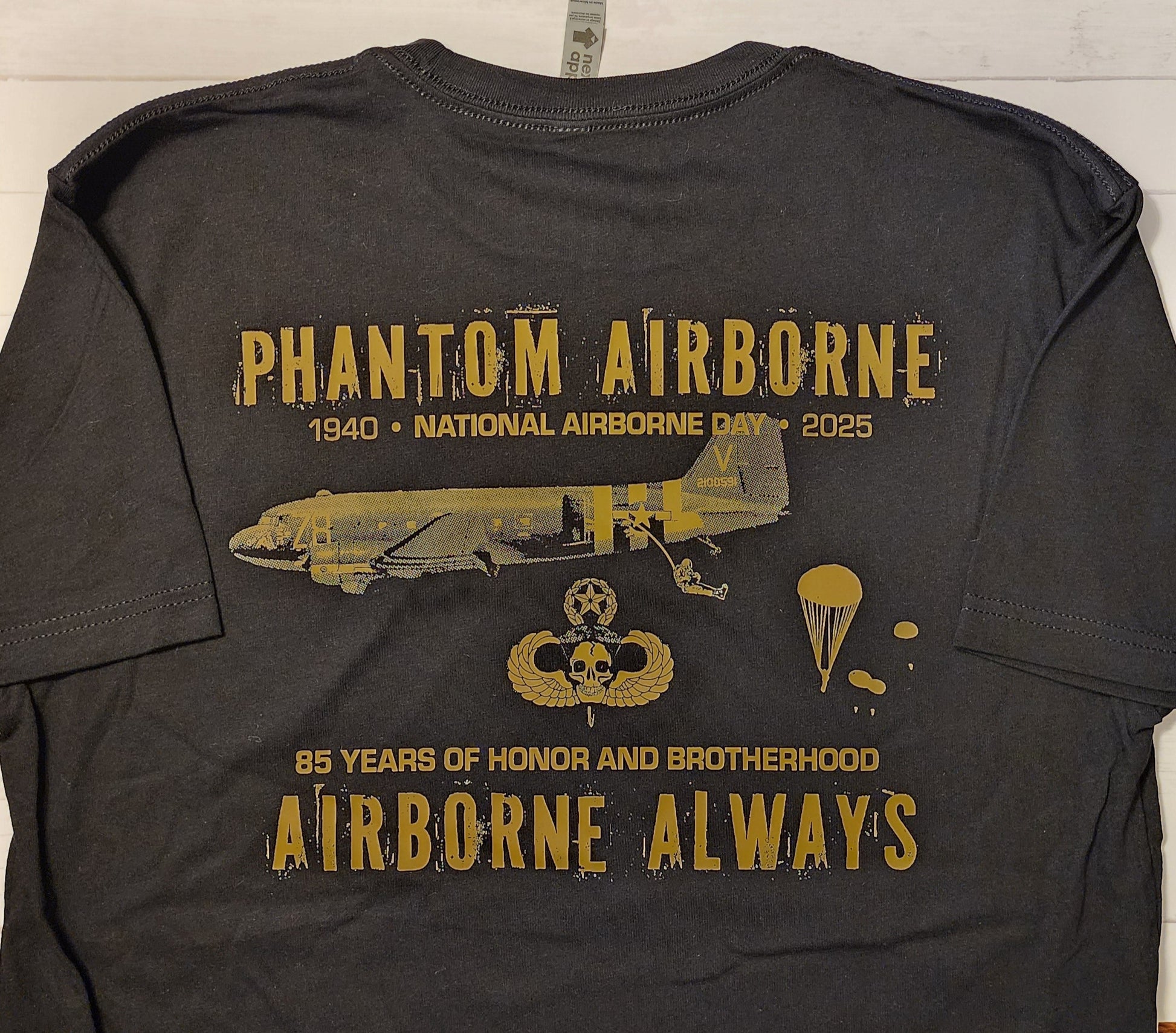 Black t-shirt with gold graphics and text on a wooden surface