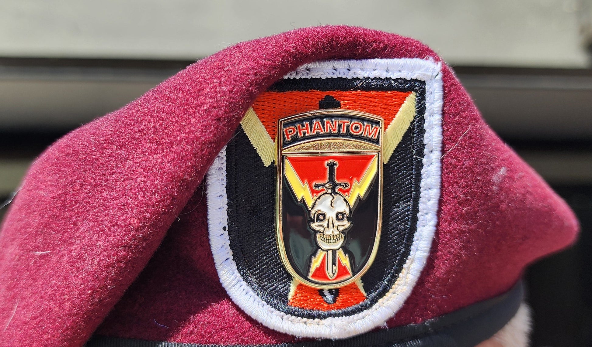 Maroon beret with a distinctive badge worn by a person, with a blurred background.