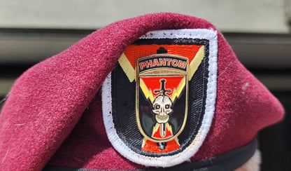 Maroon beret with a distinctive badge worn by a person, with a blurred background.