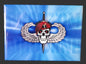 Pin with skull and crossed swords design on a blue background, placed on a textured black surface.